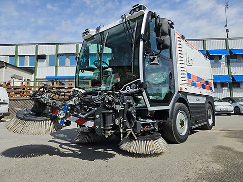 Vit sopsugmaskin med borstar framtill. 