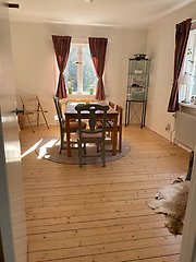 Ett rum inifrån torpet med ett bord, stolar och röda gardiner.