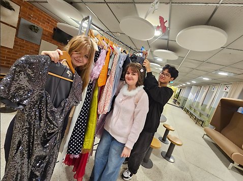 Tre elever visar upp kläder i ett uppehållsrum på Väsby skola.